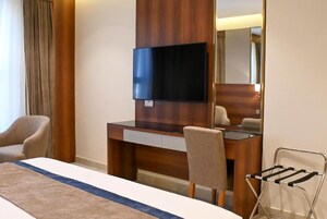 Una habitación de hotel con cama, escritorio, silla, televisor y espejo.