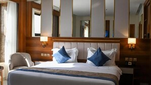 A hotel room with a large bed, two bedside lamps, a chair, and a mirror. - Corp Yanbu Hotel B2 (Yanbu)