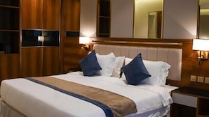A hotel room with a large bed, a wooden wardrobe, and a mirror above the bed. - Corp Yanbu Hotel B2 (Yanbu)