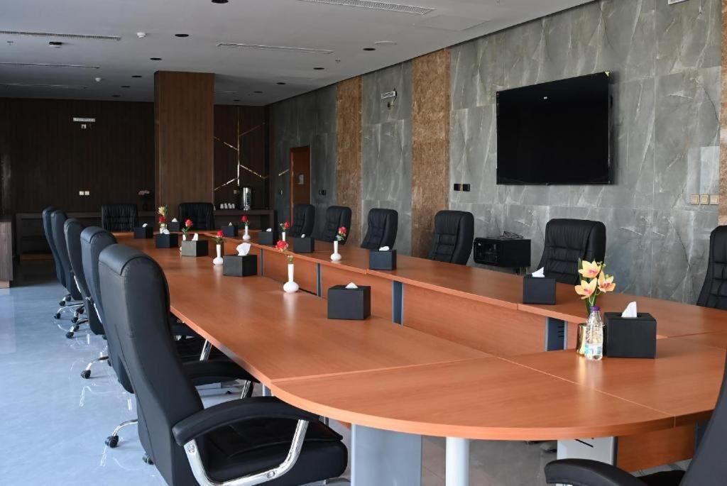 A conference room with a long table, multiple chairs, a flat-screen TV, and a decorative vase.