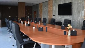 A conference room with a long table, multiple chairs, a flat-screen TV, and a decorative vase.