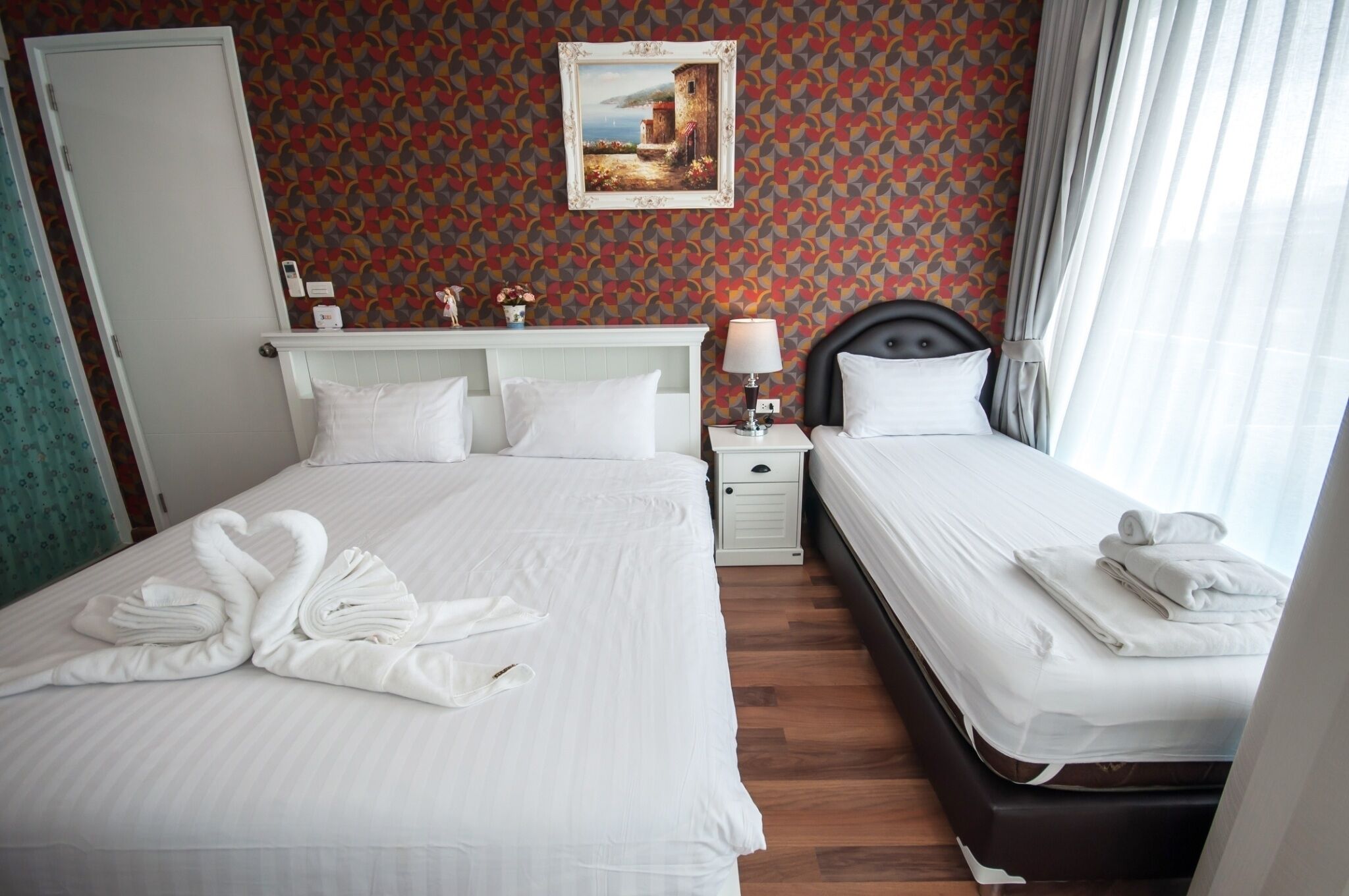 A hotel room with two beds, a painting on the wall, and a window with curtains.