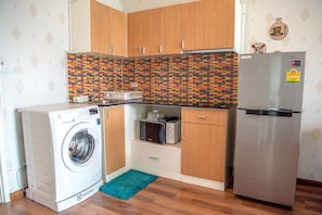 A compact kitchen with wooden cabinets, a washing machine, a microwave, and a refrigerator. - D409 Spacious 3-bedroom apartment in serene Huahin with Playground near Beach (Huahin)