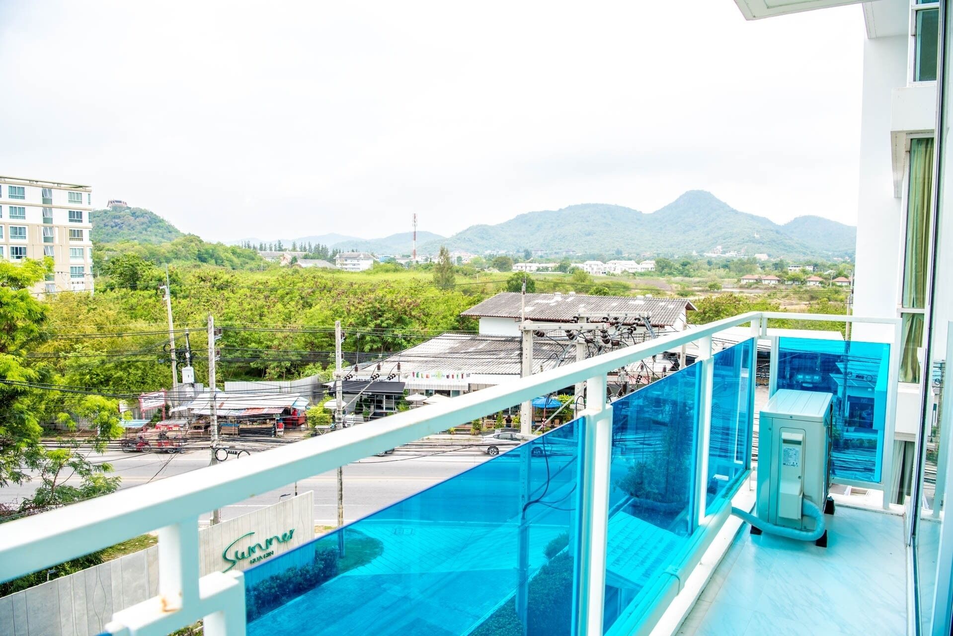 A balcony with a glass barrier overlooking a cityscape with buildings and mountains.