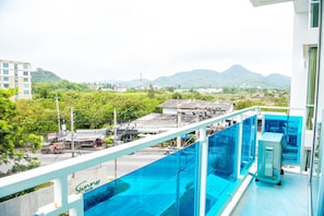 A balcony with a glass barrier overlooking a cityscape with buildings and mountains. - D409 Spacious 3-bedroom apartment in serene Huahin with Playground near Beach (Huahin)