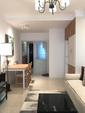 A modern living room with a sofa, a dining table with chairs, a coffee table, a chandelier, and a kitchen area with cabinets and a refrigerator. - Innocondo Extended Stay Changning  West Yan'an Road (Shanghai)
