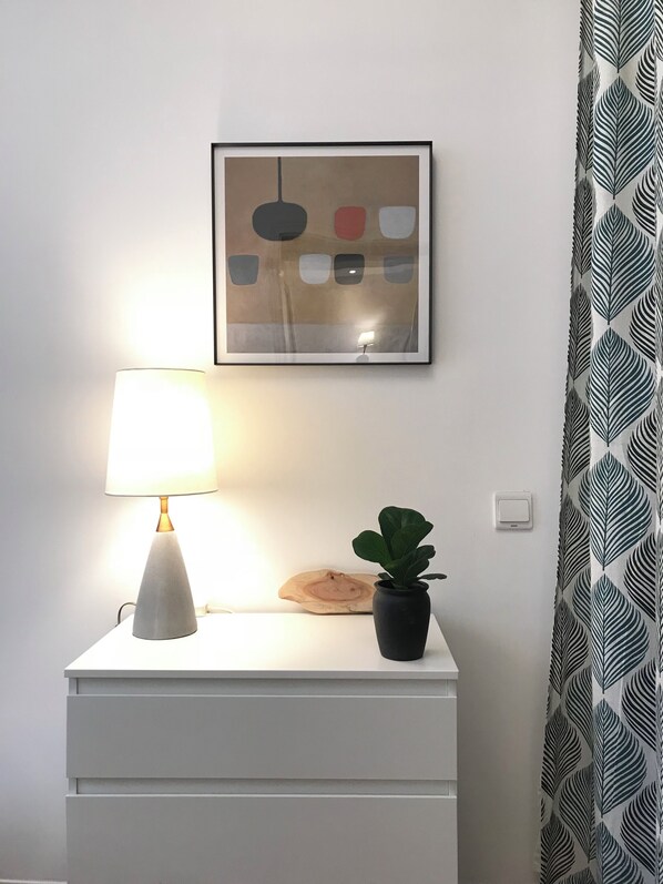 A bedside table with a lamp, a framed abstract artwork, and a potted plant.