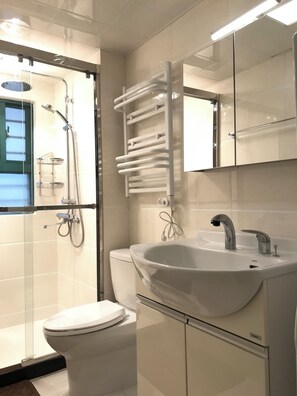 A modern bathroom with a glass shower enclosure, a white sink with a mirror above, and a toilet. - Innocondo Extended Stay West Yan'an Road (Shanghai)