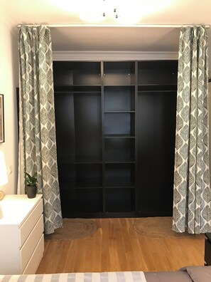 A room with a wooden floor, a bed with a striped bedspread, a bedside table with a lamp, a potted plant, and a wardrobe with patterned curtains. - Innocondo Extended Stay Changning  West Yan'an Road (Shanghai)