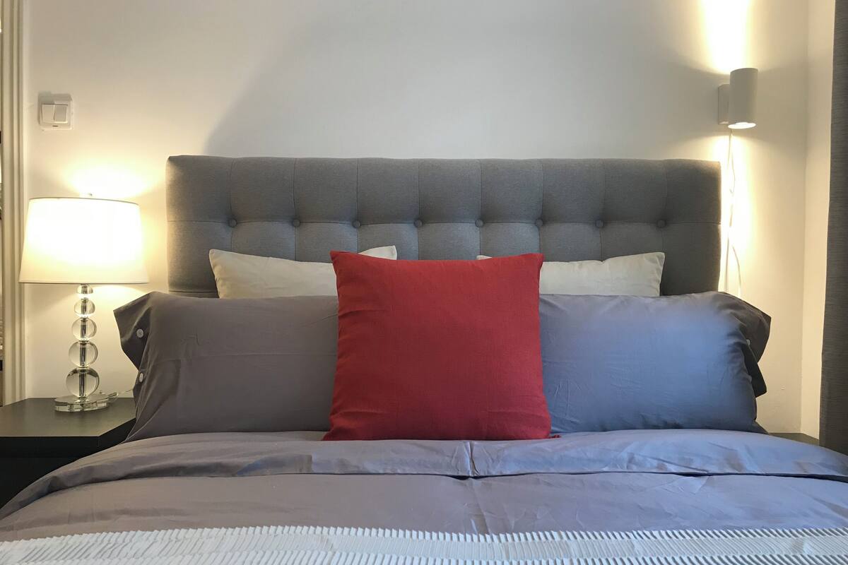 A bed with a grey headboard, white and red pillows, and a grey bedspread.