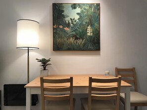A dining area with a table, chairs, a lamp, and a framed painting.