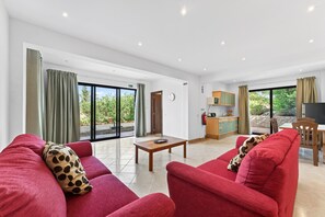 Ein geräumiger Wohnbereich mit roten Sofas, einem Holztisch und einer Küche im Hintergrund.