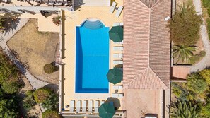 Ein Luftbild eines Hotels mit einem zentral gelegenen Schwimmbecken, umgeben von Liegestühlen und Sonnenschirmen.