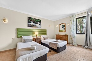 A hotel room with two beds, a green headboard, a painting of a waterfall, a wooden dresser, and a window with curtains. - Quinta dos Loendros |  9 bedrooms | Carvoeiro | Jacuzzi (Lagoa)