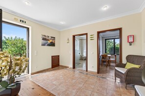 A spacious room with a large window, a door leading to a bathroom, and a dining area with a wicker sofa. - Quinta dos Loendros |  9 bedrooms | Carvoeiro | Jacuzzi (Lagoa)