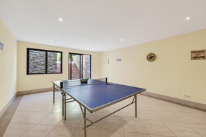 Una stanza con tavolo da ping pong, finestra vista su un muro di mattoni e vegetazione, e un pannello vintage con una targa a forma di auto da corsa.
