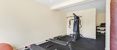 Ein Fitnessraum mit Trainingsgeräten, einer Bank und einem Spiegel.