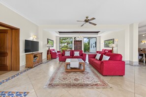 A spacious living room with a large red sofa set, a wooden coffee table, and a ceiling fan. - Quinta dos Loendros |  9 bedrooms | Carvoeiro | Jacuzzi (Lagoa)