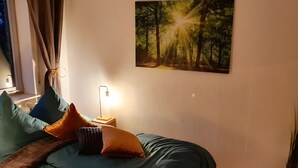A bedroom with a bed, pillows, a bedside table with a lamp, a window with curtains, and a forest-themed wall art. - Holiday at 1,000 Meters with Mountain View, Pool, Sauna, and Wi-Fi (Schönwald im Schwarzwald)