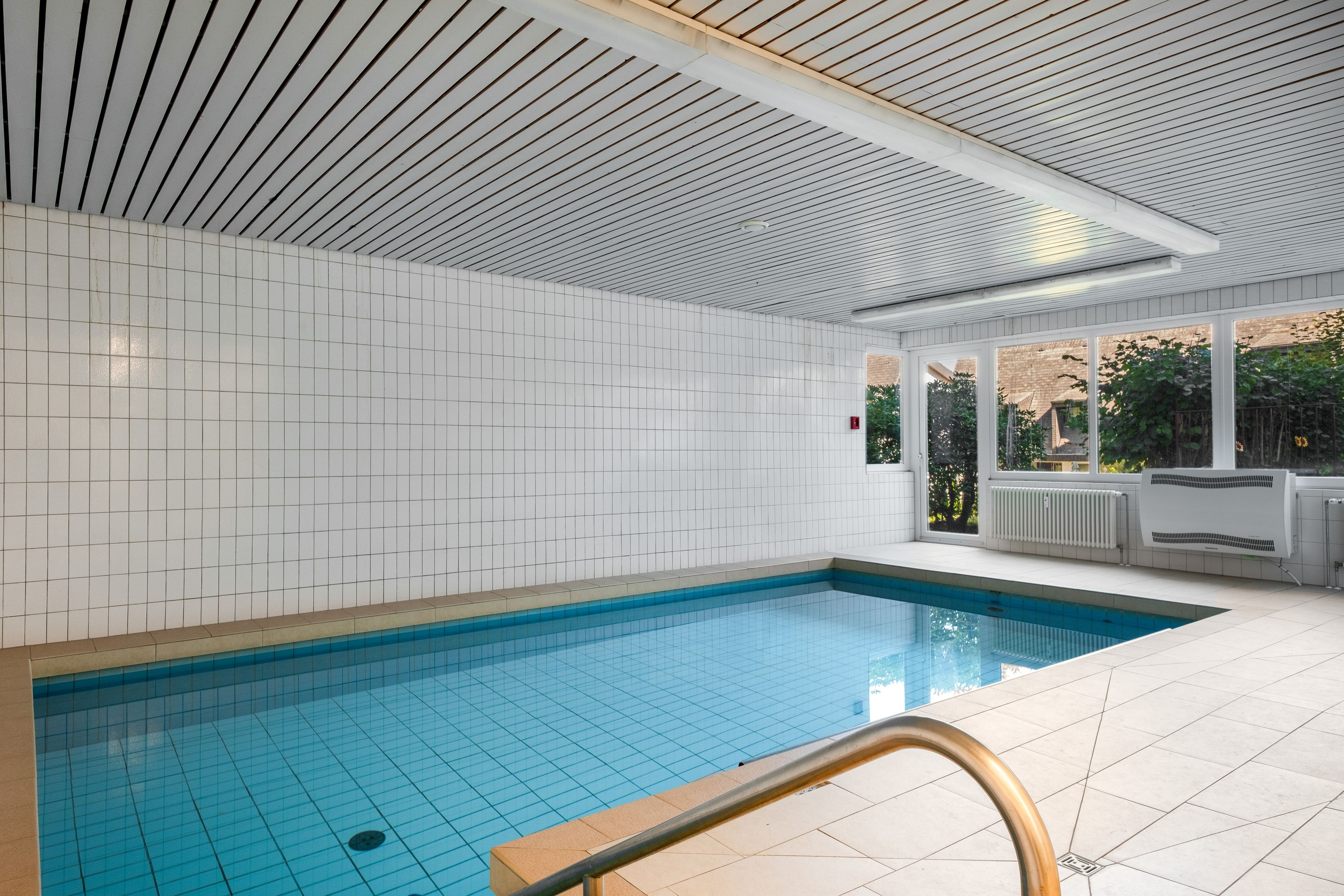 A swimming pool with tiled walls and a wooden ceiling, surrounded by a tiled floor.