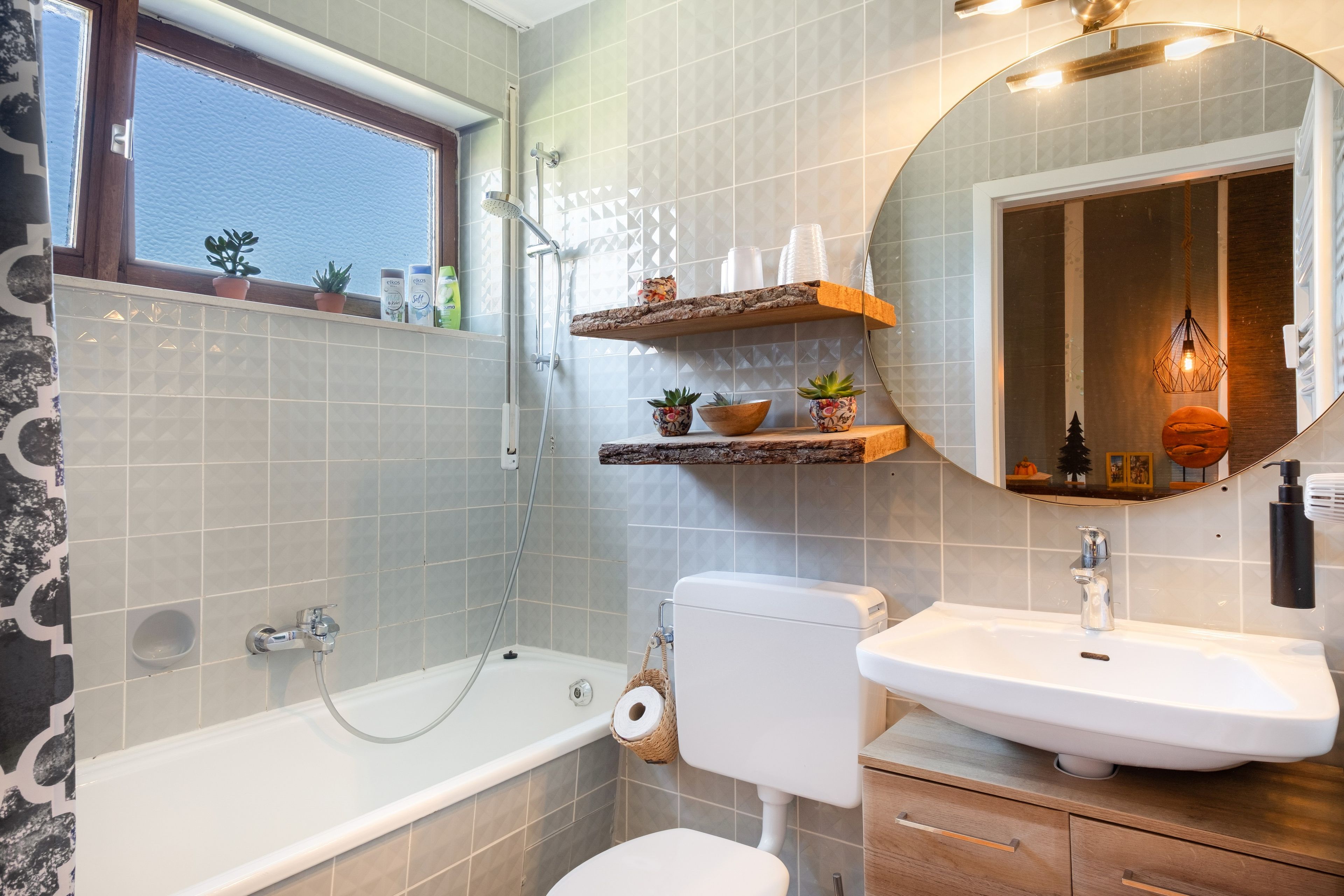 Ein Badezimmer mit Badewanne, Toilette und Waschbecken. Regale mit Toilettenartikeln und ein Spiegel über dem Waschbecken.