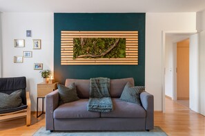 Un salon avec un canapé gris, une petite table d’appoint sur laquelle est posée une plante, et une œuvre d’art accrochée au mur.