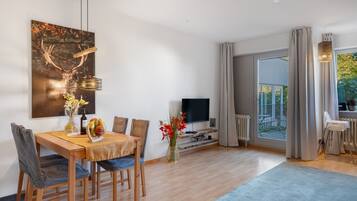 Una sala de estar moderna con comedor, televisor de pantalla plana y un amplio ventanal con cortinas.