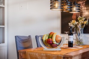 Een eettafel met een fruitschaal, een fles wijn en een vaas met bloemen.