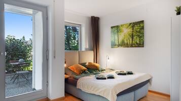 A bedroom with a bed, a window, a painting, and a view of the outdoors.