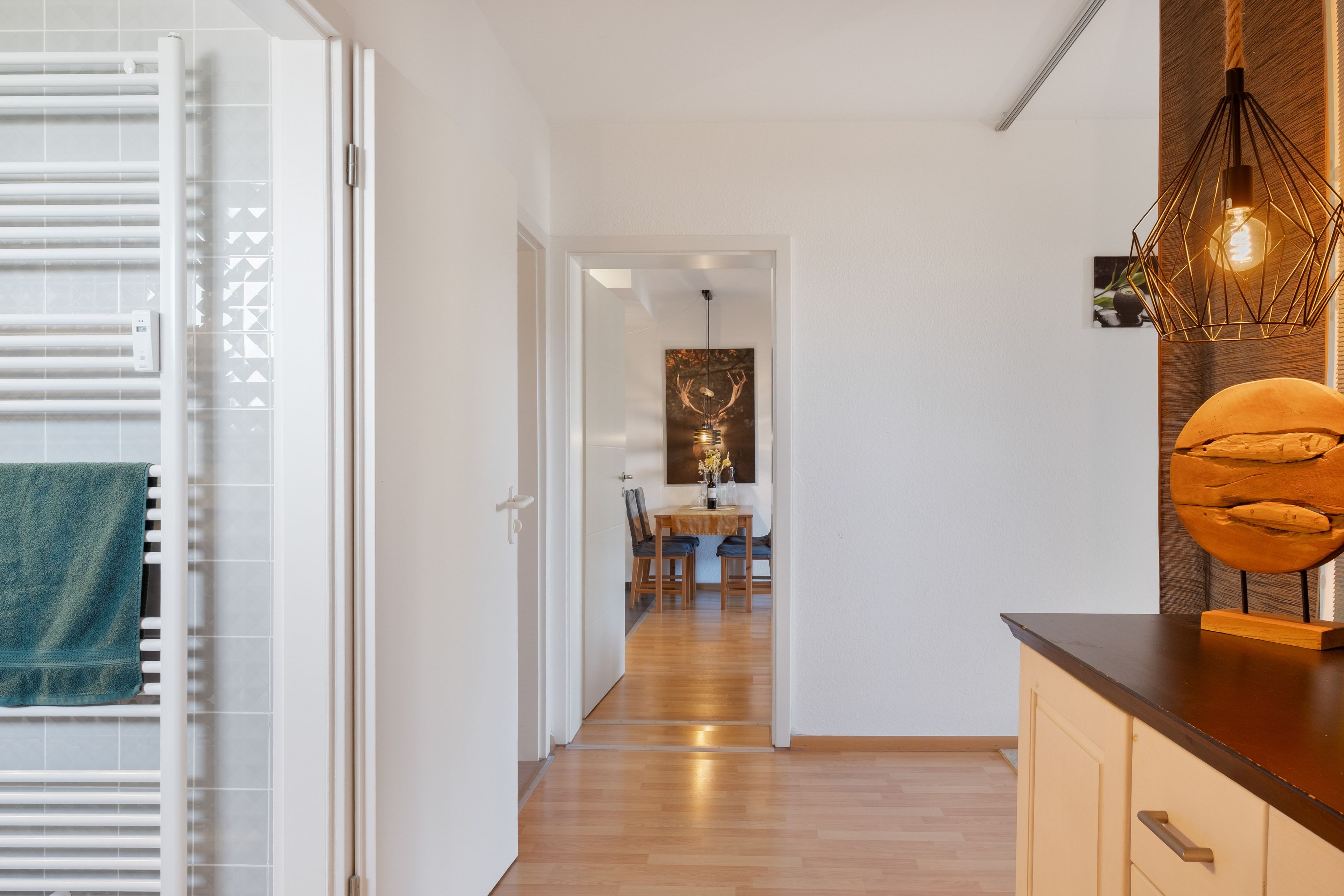 A modern interior with a wooden floor, a dining area with a table and chairs, and a kitchen area with a countertop and a hanging light fixture.