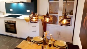 A modern kitchen with white cabinets, a black stove, and a wooden dining table set with plates, glasses, and cutlery. - Holiday at 1,000 Meters with Mountain View, Pool, Sauna, and Wi-Fi (Schönwald im Schwarzwald)