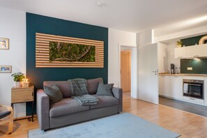 Un salon moderne avec un canapé gris, une table d’appoint en bois et une œuvre d’art murale verte.
