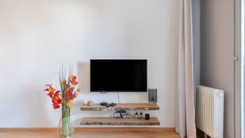Ein modernes Wohnzimmer mit einem an der Wand befestigten Flachbildfernseher, einem Holztisch, einer Blumenvase und einer Heizung.