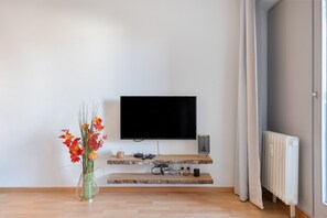 A modern living room with a flat-screen TV mounted on a wall, a wooden coffee table, a vase with flowers, and a radiator. - Holiday at 1,000 Meters with Mountain View, Pool, Sauna, and Wi-Fi (Schönwald im Schwarzwald)