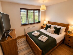 Ein Schlafzimmer mit Bett, Nachttischen, einer Lampe, einem Fernseher und einem Fenster mit Jalousien.