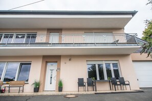 A two-story building with a balcony, a door with a number plaque, and outdoor seating.