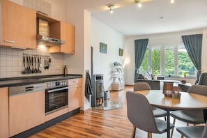 Una cocina moderna con armarios de madera, horno empotrado y zona de comedor con mesa y sillas.