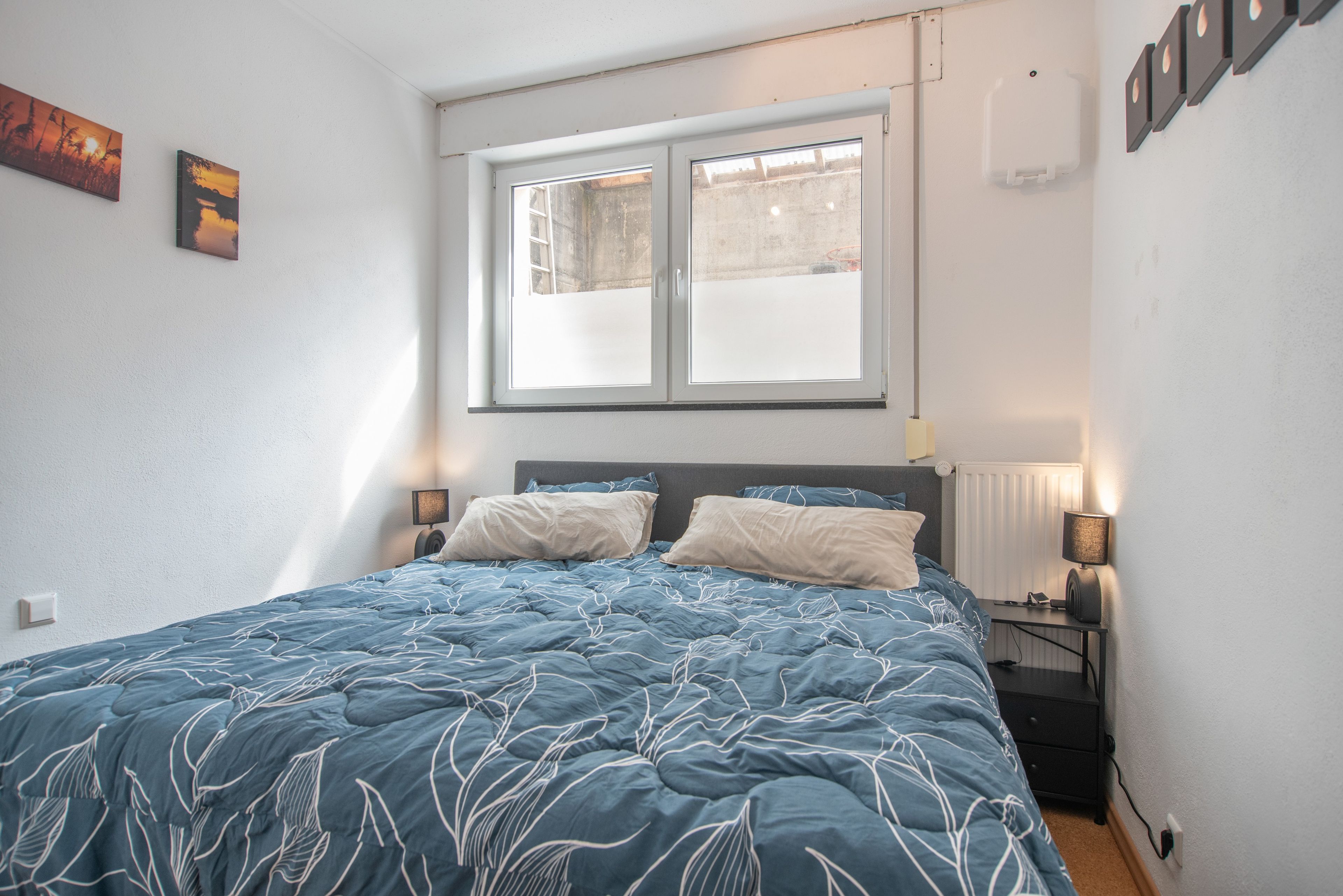 Una camera da letto con un letto, due lampade da comodino, una finestra e un termosifone.