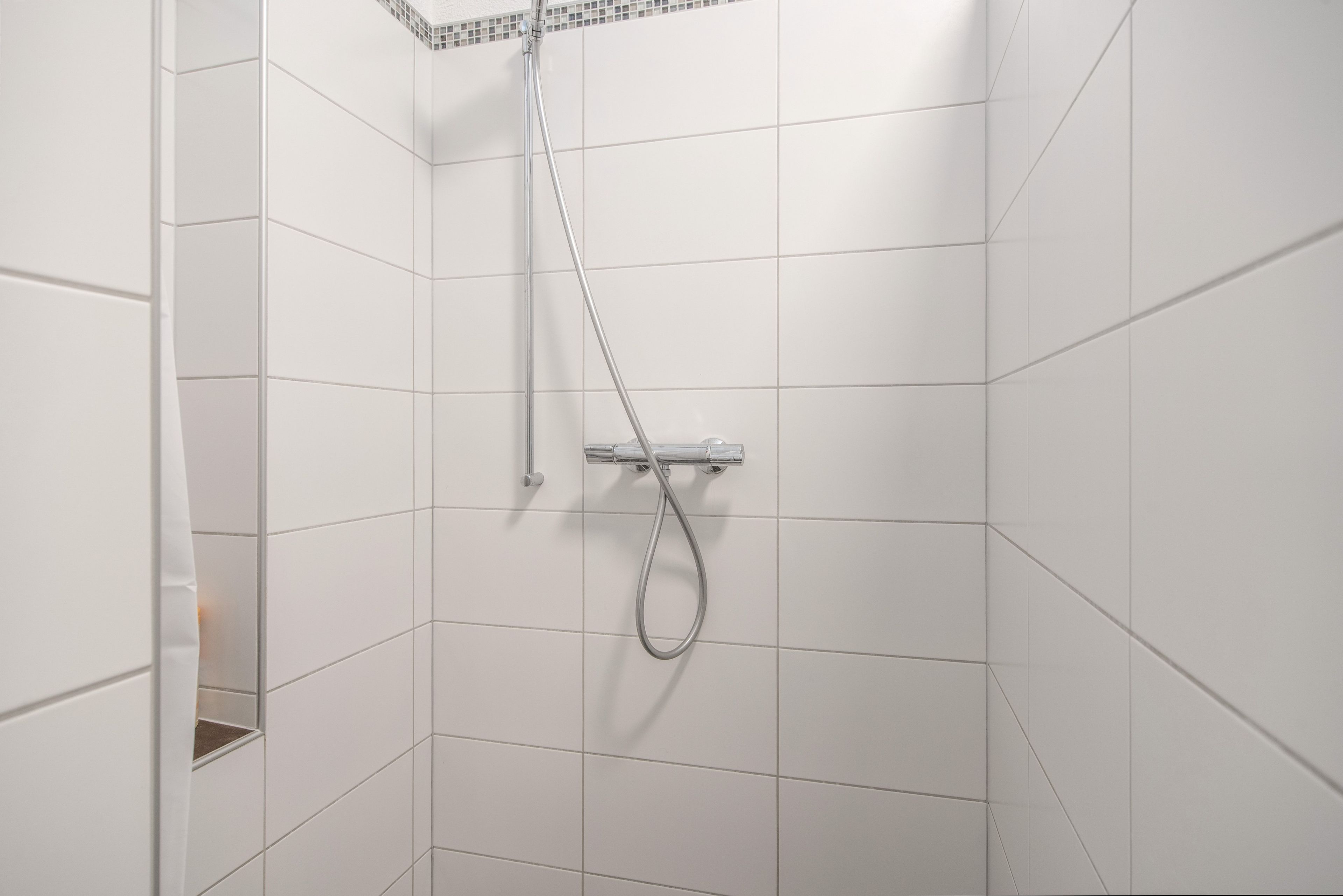 Une douche équipée d’un pommeau de douche à main et d’un robinet mural.