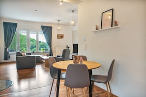 A modern living room with a round wooden table, grey sofas, and a television.