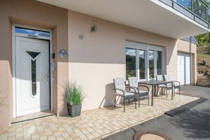 Ein Wohngebäude mit weißer Tür, einem Balkon und einer Terrasse mit Tisch und Stühlen.