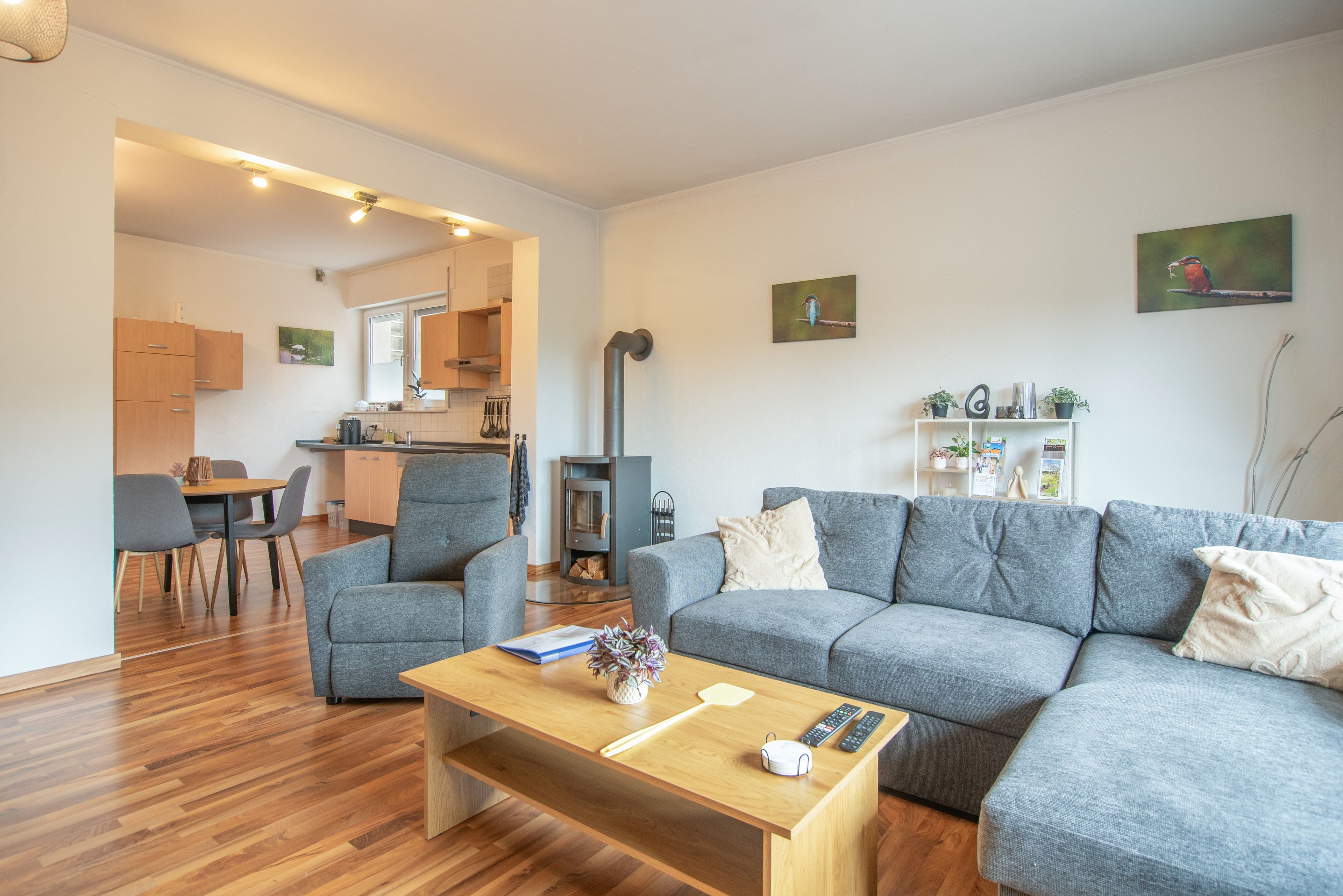 Ein modernes Wohnzimmer mit grauem Sofa, einem Holztisch und einem Essbereich mit Stühlen und Tisch.