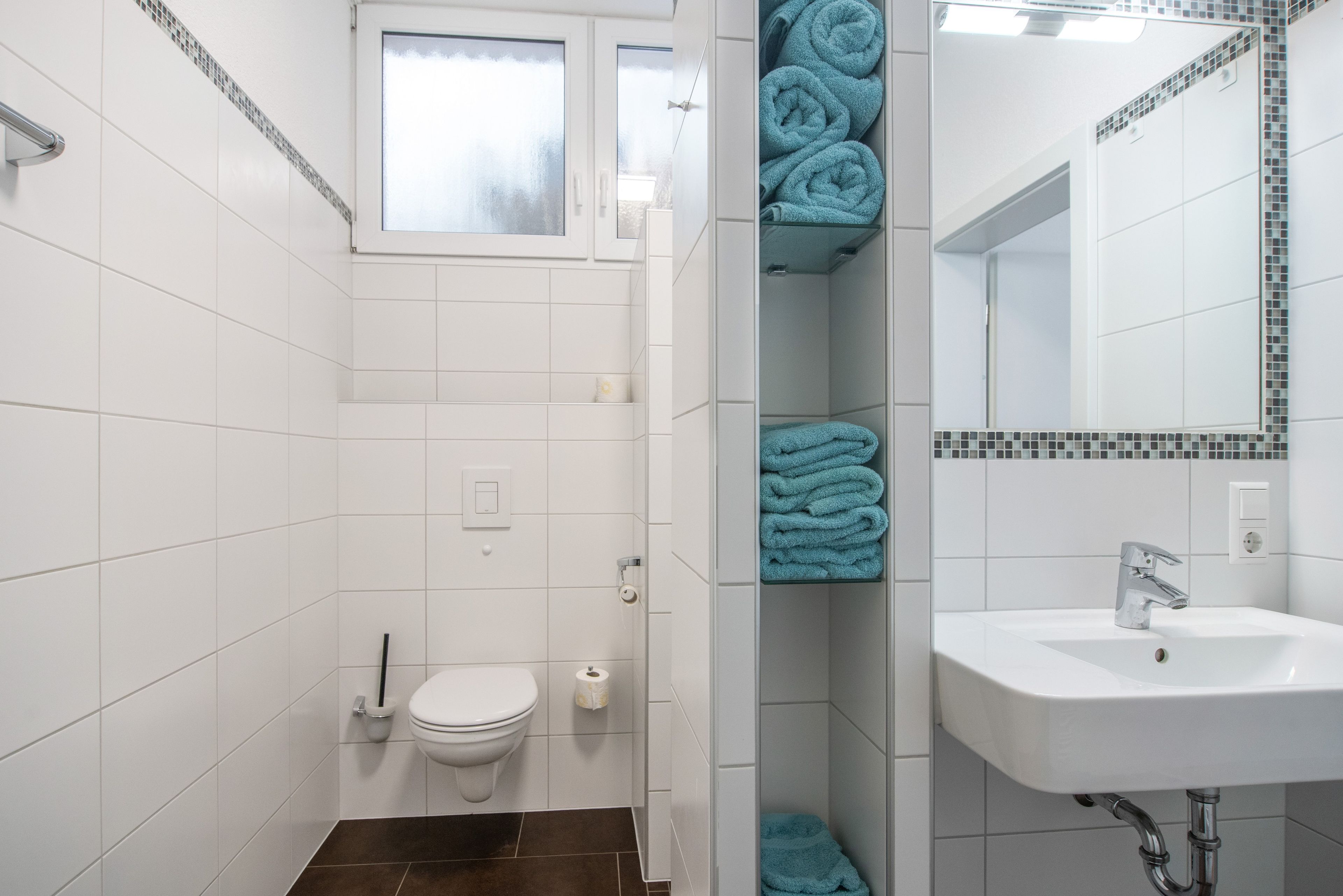 A bathroom with white tiled walls, a white sink, a toilet, and a shower area.