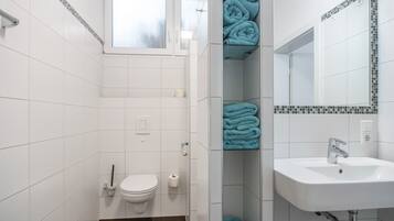 A bathroom with white tiled walls, a white sink, a toilet, and a shower area.