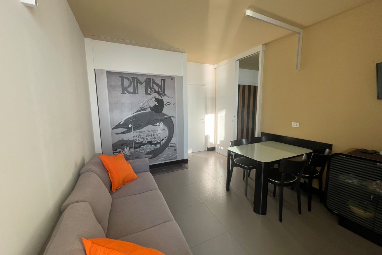Un espacio de sala de estar con un sofá, una mesa de comedor con sillas y un cartel en la pared.
