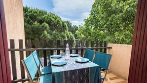 Uma área de refeições ao ar livre com uma mesa posta para quatro pessoas, cercada por cadeiras, em uma varanda com vista para árvores.