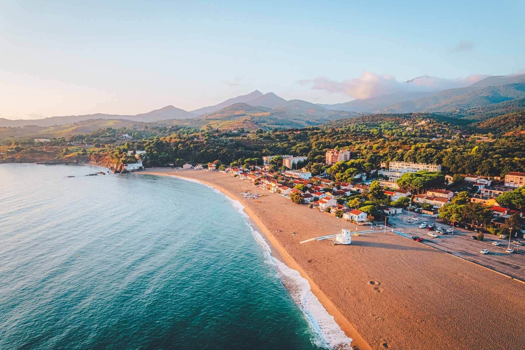 A coastal town with a beach, buildings, and mountains in the background.