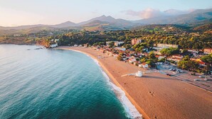 Uma vila costeira com uma praia, edifícios e montanhas ao fundo.