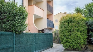Um edifício residencial com varanda curva, cerca verde e um jardim bem cuidado.