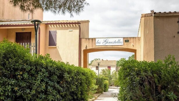 Um portão de entrada com uma placa indicando 'les Ginesettes' que dá acesso a um edifício com telhado em azulejos.